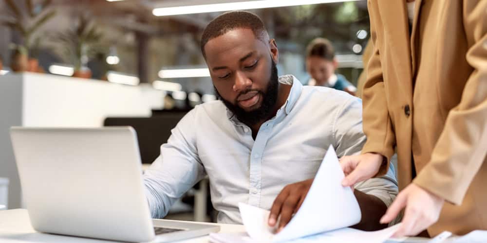 Young afro american man discussing project reports with his colleague while working together in the modern office. Team. Office life. Work concept