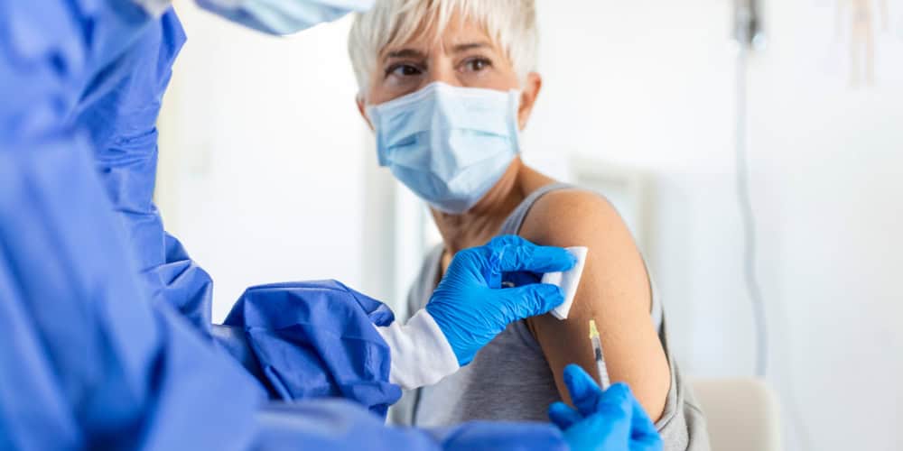 Doctor holding syringe making covid 19 vaccination injection dose in shoulder of female patient wearing mask. Flu influenza vaccine clinical trials concept, corona virus treatment, close up view.